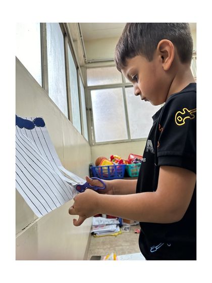 We provide careful guidance during scissor practice. This activity is crucial for developing the precision and control needed for pre-writing skills and other detailed tasks.