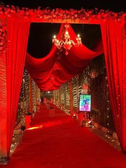A classic wedding entrance with a red carpet and red drapes. The chandelier at the entrance and the fairy lights along the walkway add a warm and inviting glow.