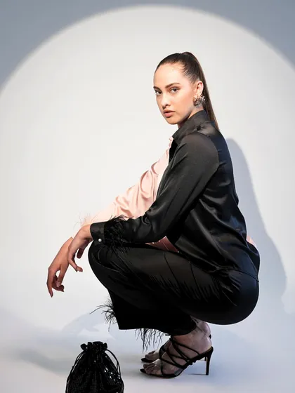 This look features a unique two-toned satin shirt with feather-trimmed cuffs. The crouching pose highlights the texture and detail of the trousers and shirt.