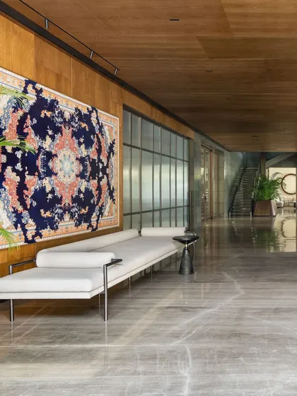 The long, gallery-like entrance lobby of the K Residence, with oak veneer paneling and polished marble floors. A long daybed sits opposite a vibrant artwork, creating a space that is both a passageway and a destination.