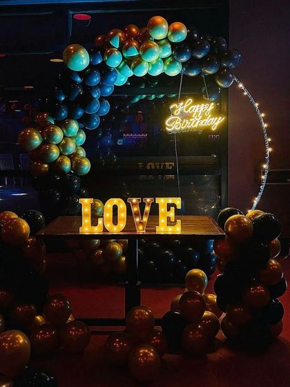 A moody and stylish balloon decoration for an evening party. The dark balloons, neon sign, and marquee 'LOVE' letters create a cool and intimate atmosphere.