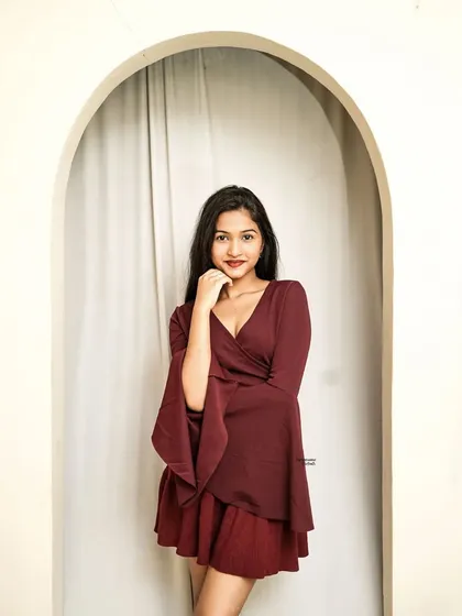 A welcoming pose in an arched doorway, the model's smile and the flowing sleeves of her maroon outfit create a beautiful frame.