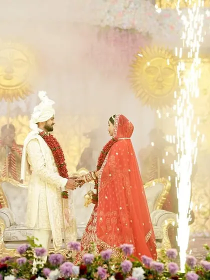 A romantic Jaimala moment, with the couple framed by golden pyrotechnic sparks. The soft lighting and traditional props create an intimate yet spectacular setting for their union.