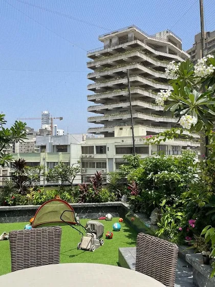 A family's terrace garden designed to be both beautiful and functional. We used durable artificial turf for a play area, surrounded by lush planters filled with flowering trees and shrubs, creating a safe and green space against the Mumbai skyline.