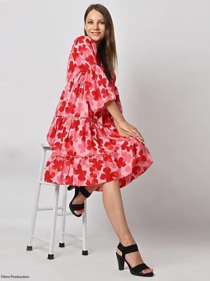 A seated pose in a vibrant pink and red floral dress. This lifestyle shot adds personality and context, helping customers envision wearing the dress for various occasions.