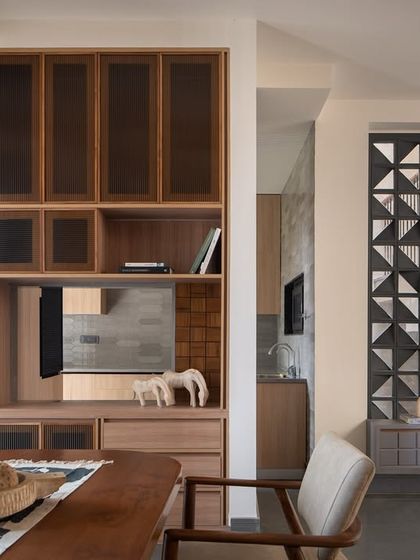 The custom shelving unit flows from the dining area into the kitchen, creating a visual spine that connects the shared spaces. The design is both a storage solution and a key part of the home's spatial navigation.