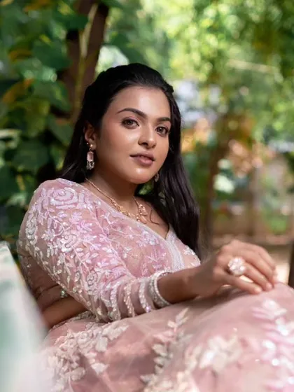 A serene shot of a model in a pink lehenga, sitting on a bench. The makeup is subtle and elegant.