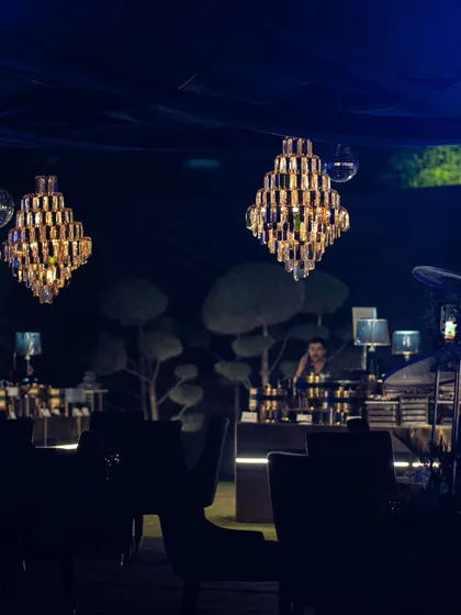 An atmospheric shot of the Diwali party, with crystal chandeliers hanging under a dark canopy, creating a moody and luxurious outdoor lounge.
