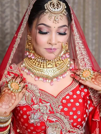 A bride in a red lehenga wearing a gold-plated choker with pink bead drops. The oversized maang tikka and rings complete this grand bridal look.