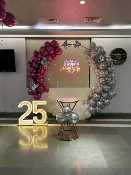 Another view of the 25th-anniversary setup, showing how the pink lighting enhances the magenta and silver balloons and the glowing neon sign.