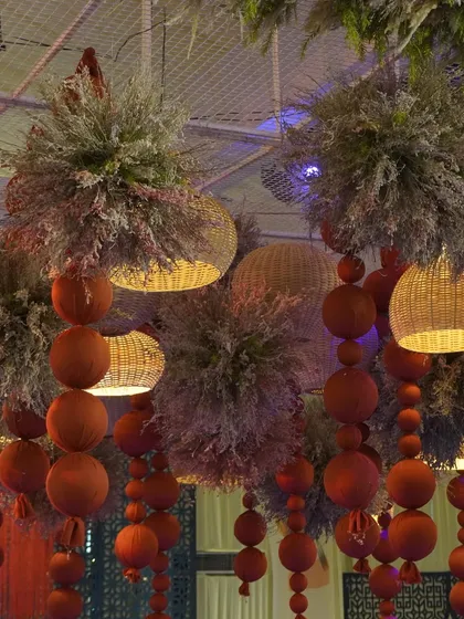 A close-up of the ceiling installation at the 'Moroccan Nightfall' event, with pampas clouds, cane lamps, and hanging orange spheres.