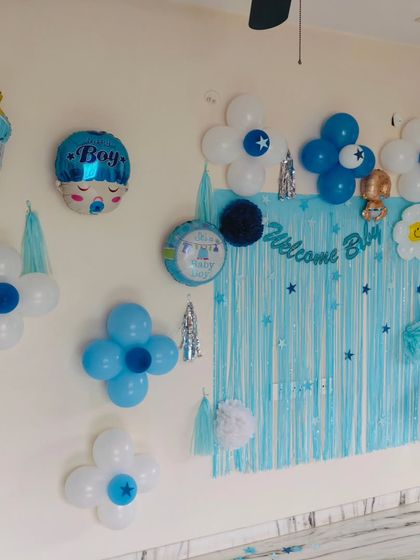 A sweet and simple "Welcome Boy" wall decoration. This setup is perfect for a more intimate home celebration, featuring a blue foil curtain and flower-shaped balloon clusters.