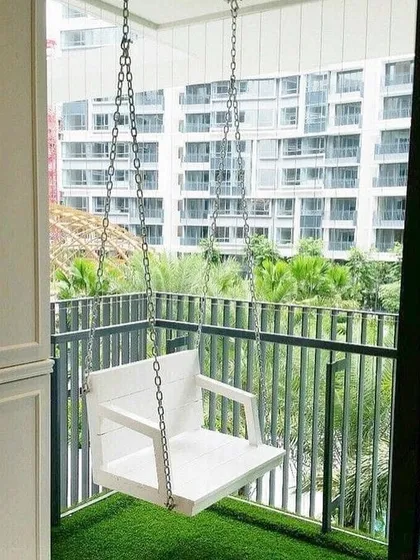 A simple, clean design for a small urban balcony. The main feature is a modern white swing, which provides a relaxing spot to enjoy the view. The artificial grass floor adds a touch of green and softness underfoot.