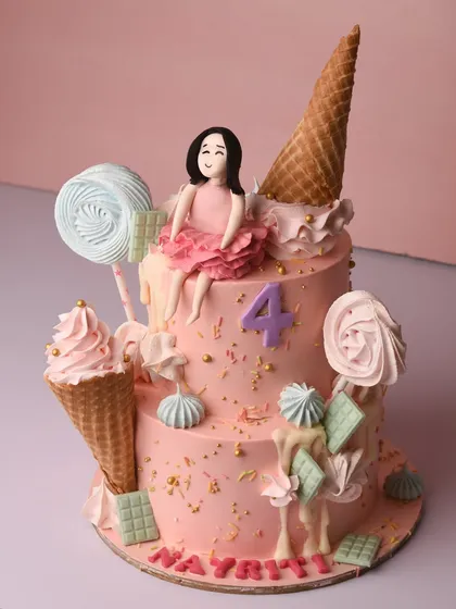 A candy lover's dream cake for a fourth birthday. This two-tier pink cake is overloaded with sweet treats, including fondant lollipops, ice cream cones, chocolate bars, and a cute little girl figurine.