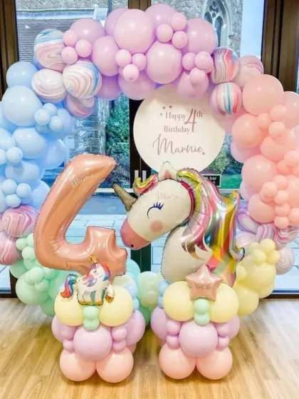 A lovely unicorn-themed birthday setup. The circular balloon arch is made of pastel rainbow colors and features a large unicorn head foil balloon as the centerpiece.