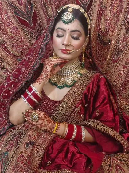 A truly royal look featuring a rich red velvet lehenga with detailed gold embroidery. The matching jewellery set with green accents completes this traditional bridal ensemble.