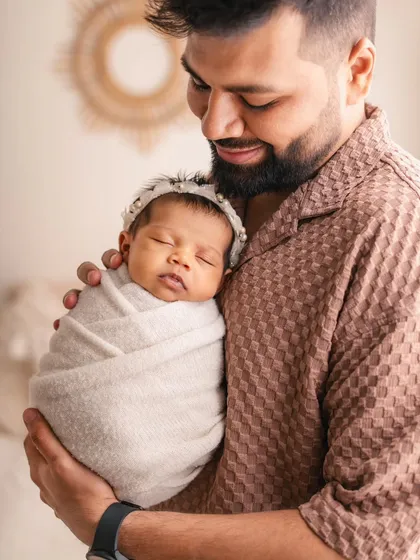 A proud father holds his peacefully sleeping newborn daughter. This close-up shot highlights the delicate features of the baby and the father's gentle hold.