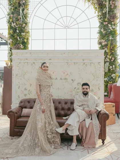 A regal portrait session. The couple, seated on a vintage sofa against a beautifully decorated backdrop, looks like modern-day royalty in their elegant reception attire.