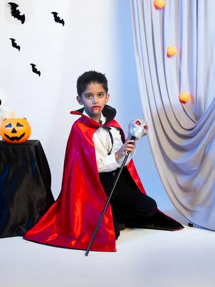 A young model dressed as Dracula in a red and black cape, holding a skull staff for a fun and theatrical Halloween product shoot.