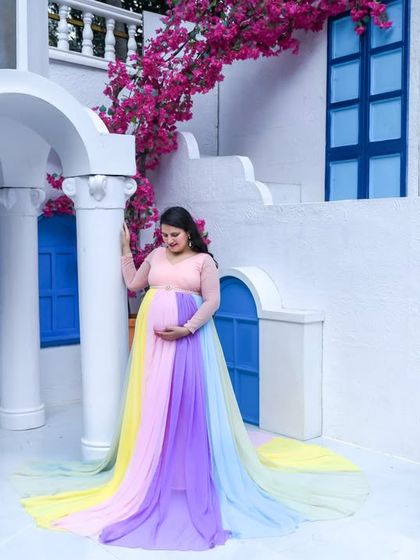 A dreamy, picturesque shot at a location that looks like Santorini. The mom-to-be in our rainbow gown stands among white walls and blue windows, creating a perfect vacation vibe.