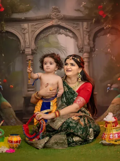 A heartwarming mother and child portrait from a Krishna-themed session. This photo captures the special bond between a mother and her baby, both dressed in beautiful traditional attire against an ornate backdrop.