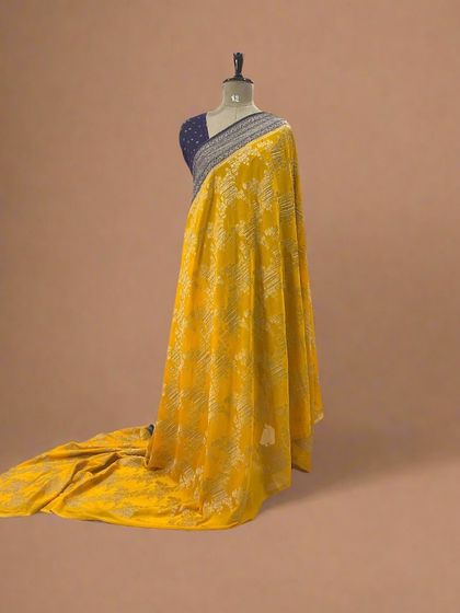 A yellow soft crepe saree with a unique silver jaal pattern and a blue border.