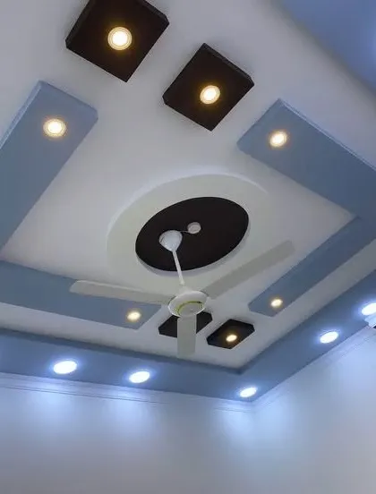A two-tone color scheme of blue and white with dark brown accents. This design shows how to integrate a ceiling fan into a modern, multi-level false ceiling.