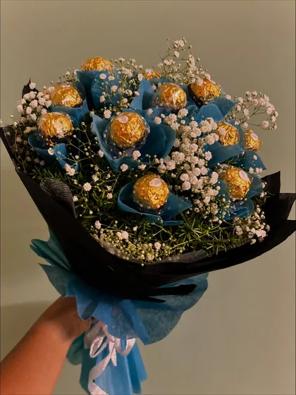 A hand-held view of the blue Ferrero Rocher bouquet, giving a sense of its size and lushness. The combination of blue, gold, and white is truly eye-catching.