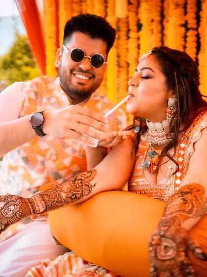 A candid moment of fun during the Mehendi ceremony, with the groom helping the bride take a sip of coconut water.