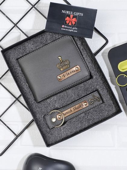 A grey leather wallet and keychain combo, personalized with a crown charm for 'Vasu'.
