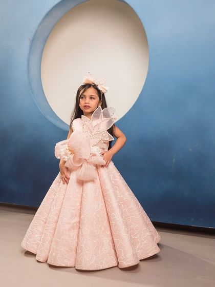 A stunning pink gown with a large, structured bow and floral detail, crafted from a beautiful brocade fabric.