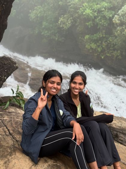 Two friends give a peace sign while sitting by a stream on the Bandaje trail.