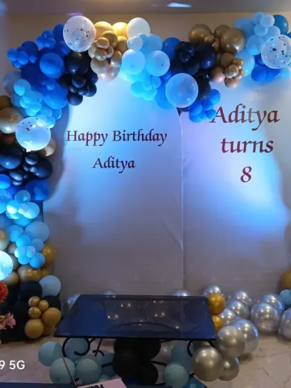 A stylish blue, black, and gold balloon arch over a simple white circular backdrop. This modern and masculine design is great for a teen or adult birthday party.