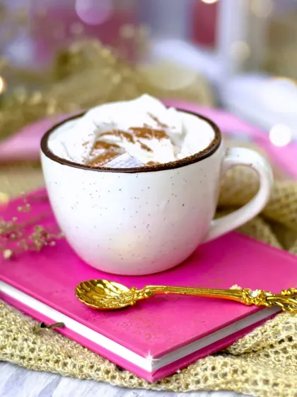 Cold weather calls for hot coffee. This cup of coffee with whipped cream is styled with a bright pink book and golden accents, creating a cheerful and cozy image.