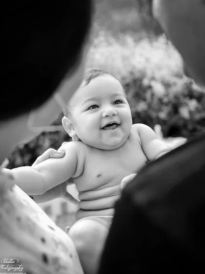 Sometimes the most powerful moments are the quiet ones. This black and white portrait, shot from over the parents' shoulders, focuses entirely on the baby's happy expression and the loving bond of this new family. These are the moments that become timeless treasures.