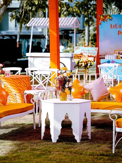 A relaxed guest seating area with white wrought-iron furniture and bright orange cushions, perfect for a sunny outdoor fiesta.