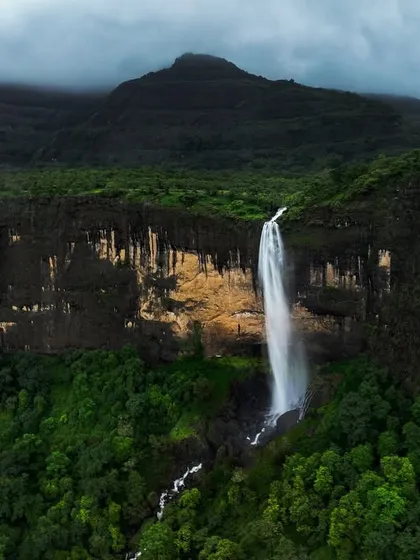 Daityasur Waterfall with the peak of a mountain shrouded in mist in the background. This composition adds a layer of mystery and grandeur to the scene.