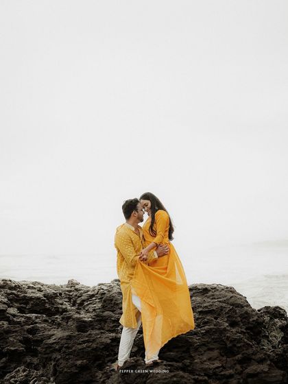 Aiswarya and Vishnu embracing on the rocks, with the sea behind them. The dramatic landscape adds a powerful, epic feel to their pre-wedding portraits.