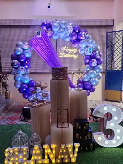 A third birthday party at home, using a purple and silver balloon ring and marquee letters to create a festive corner.