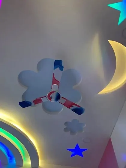 A dreamy sky-themed ceiling for a kid's room. It features a backlit crescent moon, stars, and a cloud-shaped base for the fan, all brought to life with colorful lights.