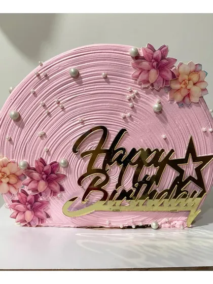 A pretty pink top forward cake with a textured swirl finish. The design is completed with edible flowers and a golden "Happy Birthday" topper.