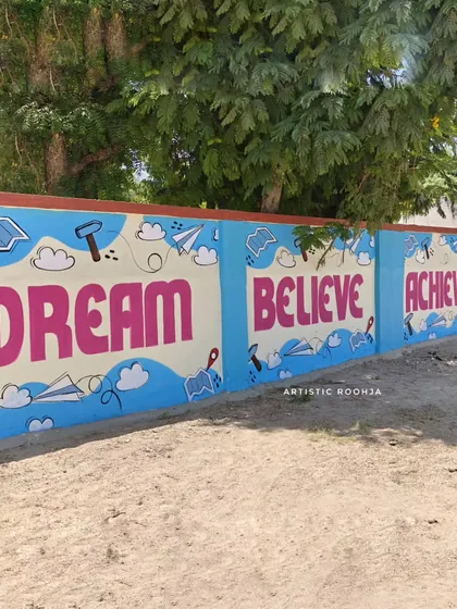 This "Dream Believe Achieve" mural is set against a sky-blue background with doodles of paper planes and books, symbolizing the journey of learning.