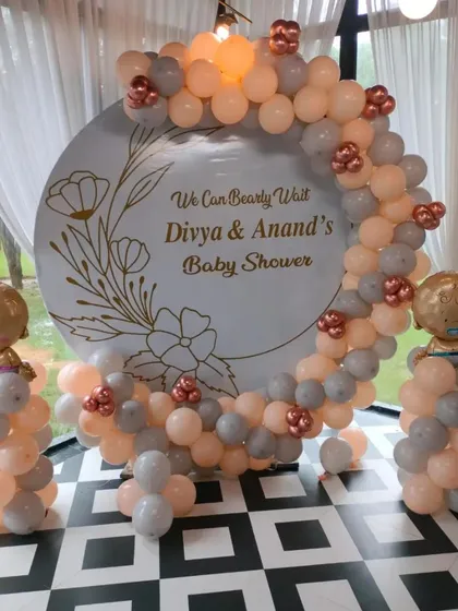 A personalized "We Can Bearly Wait" baby shower backdrop for Divya and Anand. This elegant design uses a neutral color palette of peach and grey balloons around a custom printed circular backdrop.