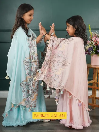 Two sisters playing in their flowing cape gowns. The delicate floral print and tassel details on the capes add a touch of magic to these pastel outfits.