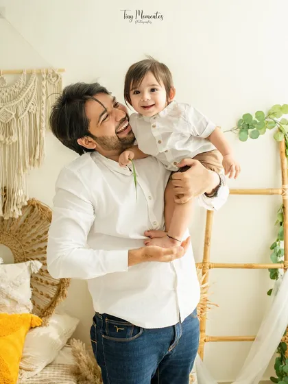 A cheeky grin from this little boy as he sits on his dad's shoulder. This playful interaction makes for a heartwarming father-son portrait.