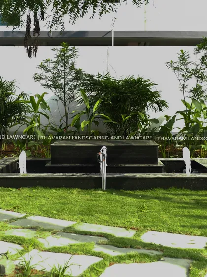 A frontal view of the black stone, multi-tiered water fountain, surrounded by a lush lawn and tropical foliage.