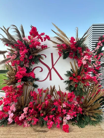 A sunny day in Doha calls for a beautiful photo-op. The couple's monogram is framed by a wreath of red flowers and pampas grass, creating a modern and chic look. 🌺