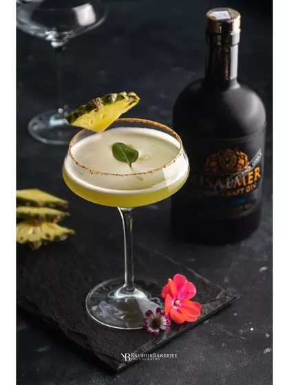 A pineapple gin cocktail, expertly garnished and ready to be served. This image, shot for Whiskey Amour, uses a dark setting to make the drink's color and form stand out.