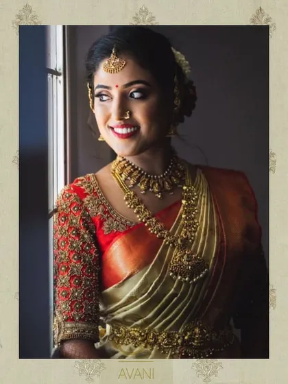 A bride wearing a vibrant red blouse with heavy gold embroidery on the sleeves. The design is a classic choice for a traditional South Indian muhurtham ceremony.