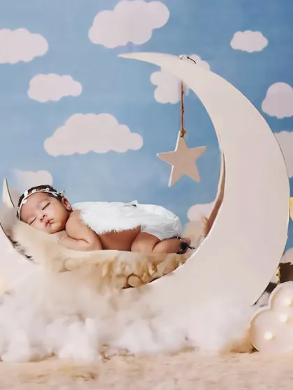 A dreamy newborn photo with the baby sleeping on a moon prop, surrounded by fluffy clouds and glowing stars.